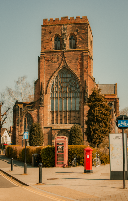 A historic church interior with high, vaulted wooden ceilings supported by intricate stone arches that extend along the length of the nave. Large stained glass windows line the upper walls, allowing n