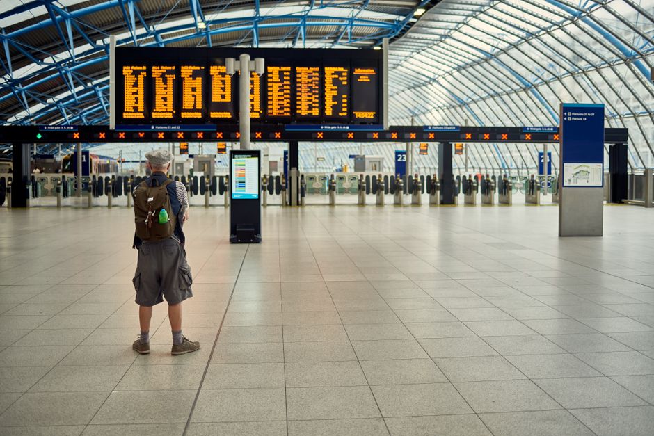 Inside a spacious underground train station with a curved platform and twin railway tracks. The station features modern lighting fixtures, including a large strip light running along the ceiling, illu